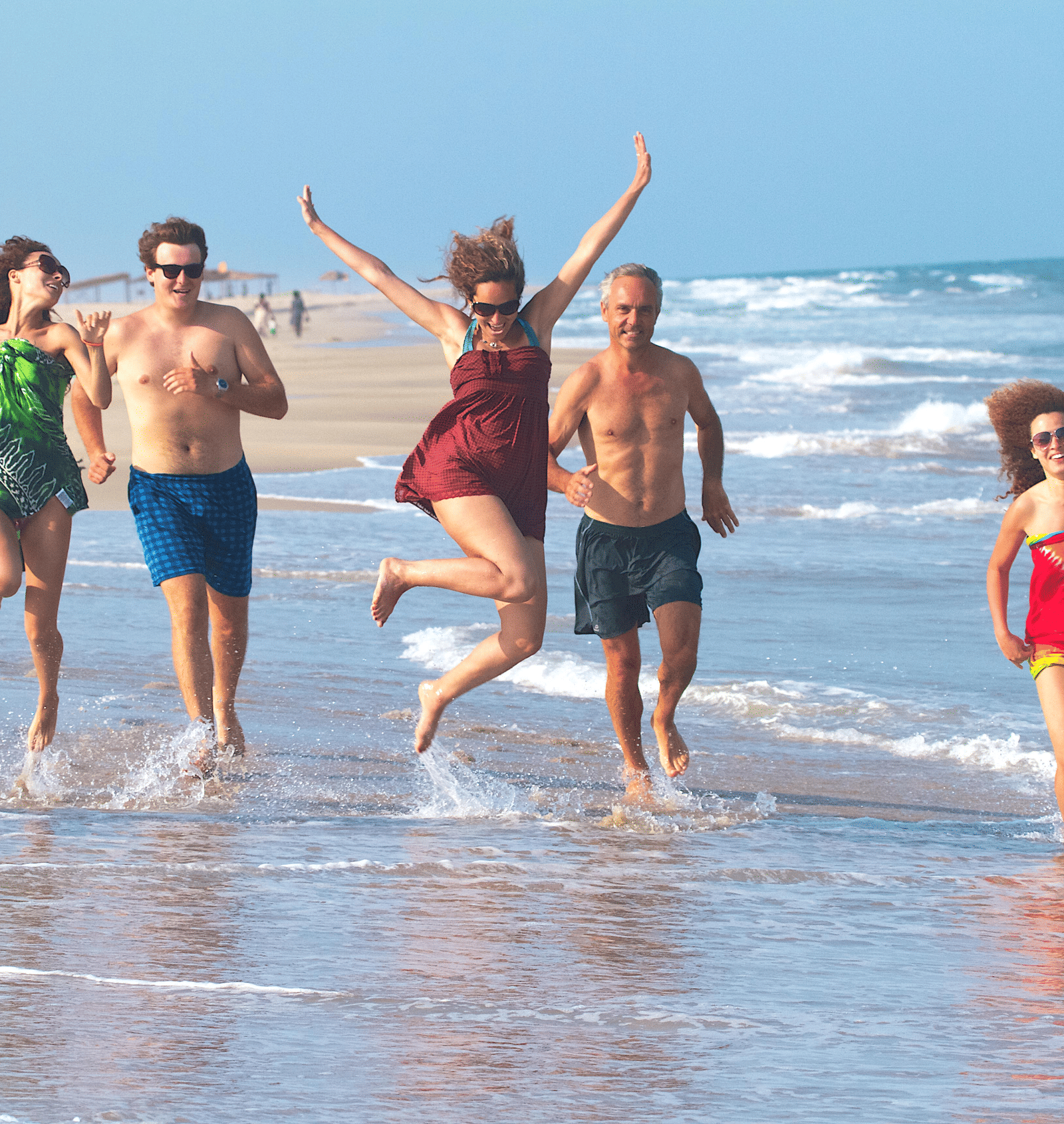 A group of 5 people running and jumping playfully along the shoreline of a sandy beach | Le Pondy