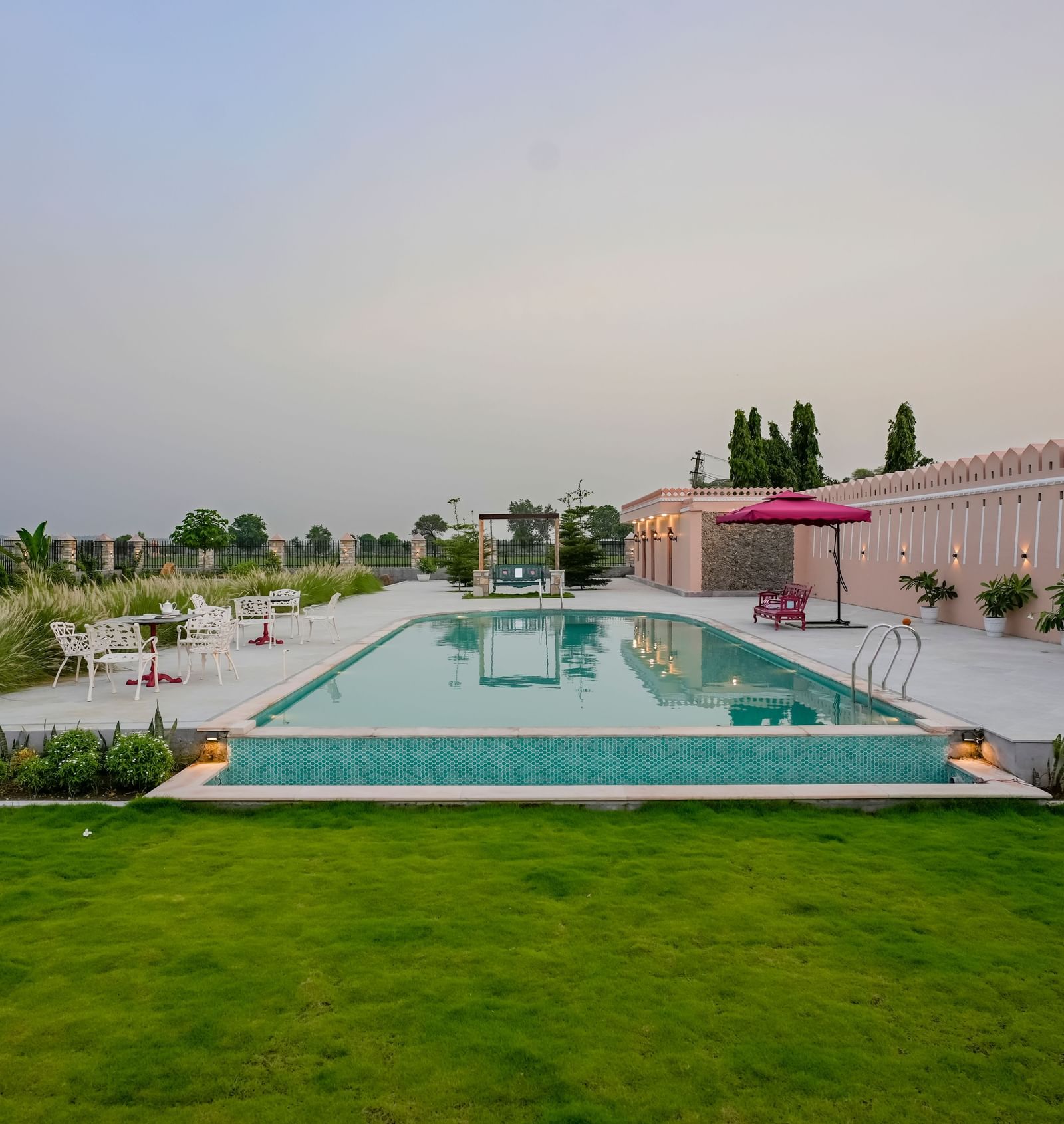 An eye-level shot of Mahendra Niwas, showcasing its luxurious swimming pool and well-maintained gardens under a soft, overcast sky.