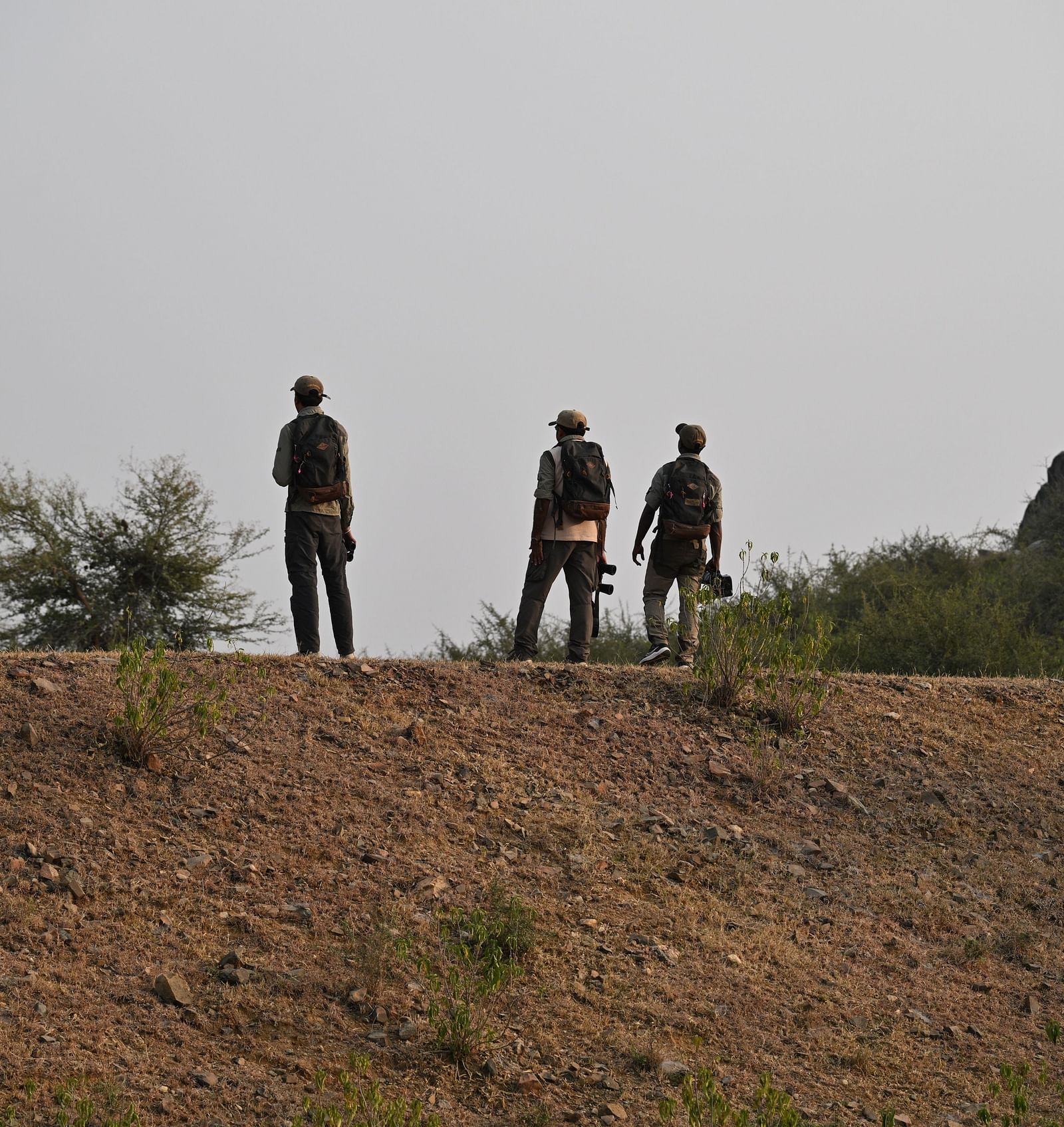 An image of three men standing on the rocky mountains - An image of a jeep parked amidst the rocky mountains - Utsav Camp Sariska