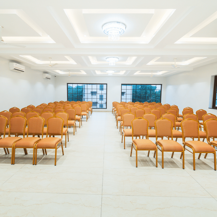 A banquet hall with orange chairs arranged in a theatre style seating arrangement - MGM Whispering Meadows
