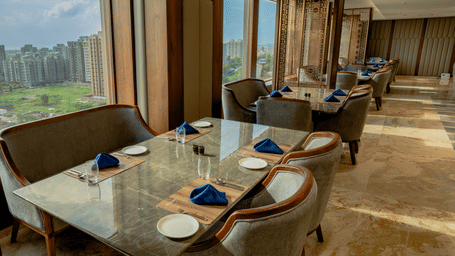 Elegant restaurant seating next to large windows offering a scenic view of the city skyline - Praveg's Grand Eulogia, Ahmedabad