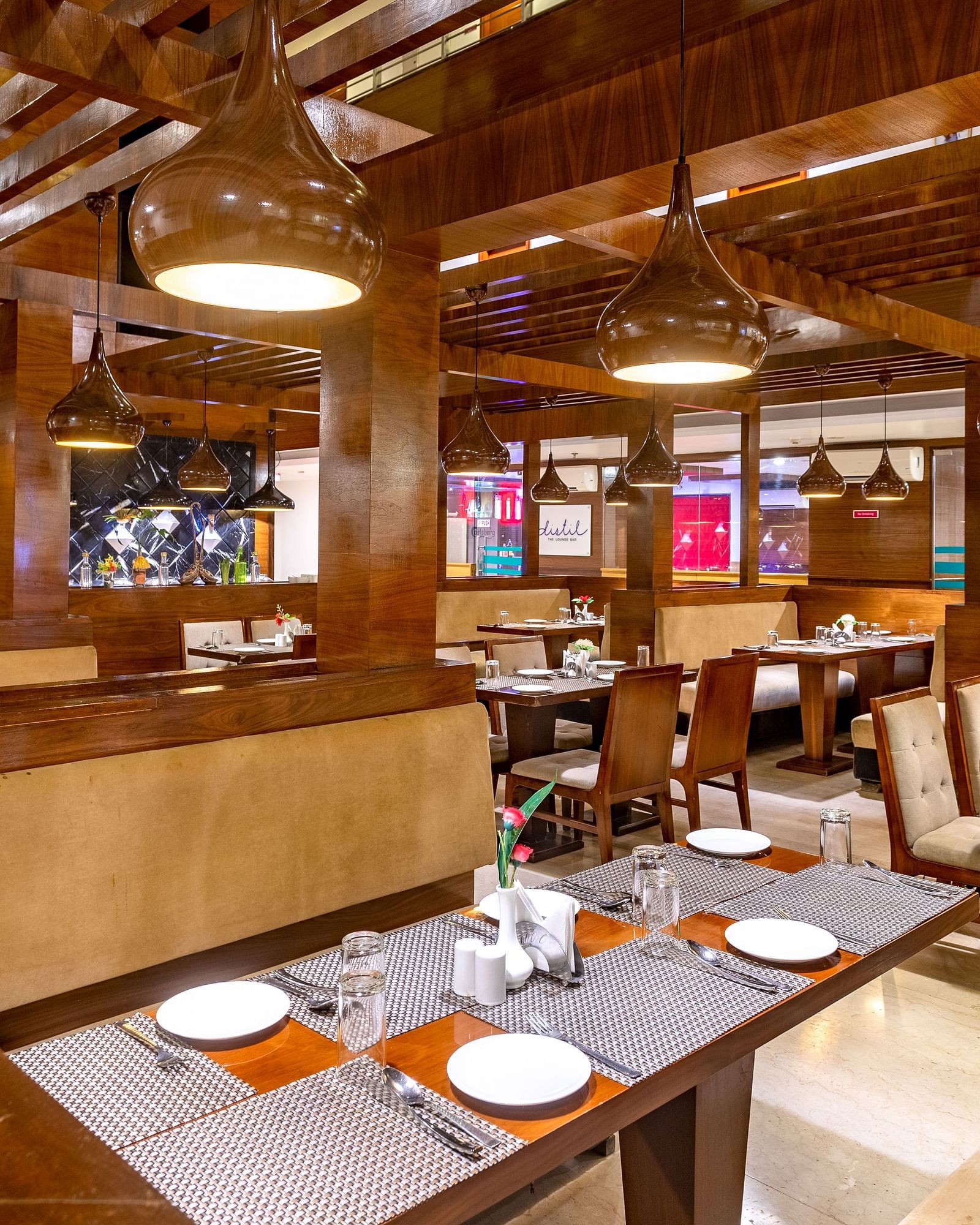 Warmly lit restaurant at Diamond Palace Lords Plaza with wooden beams, set tables, and booth seating.