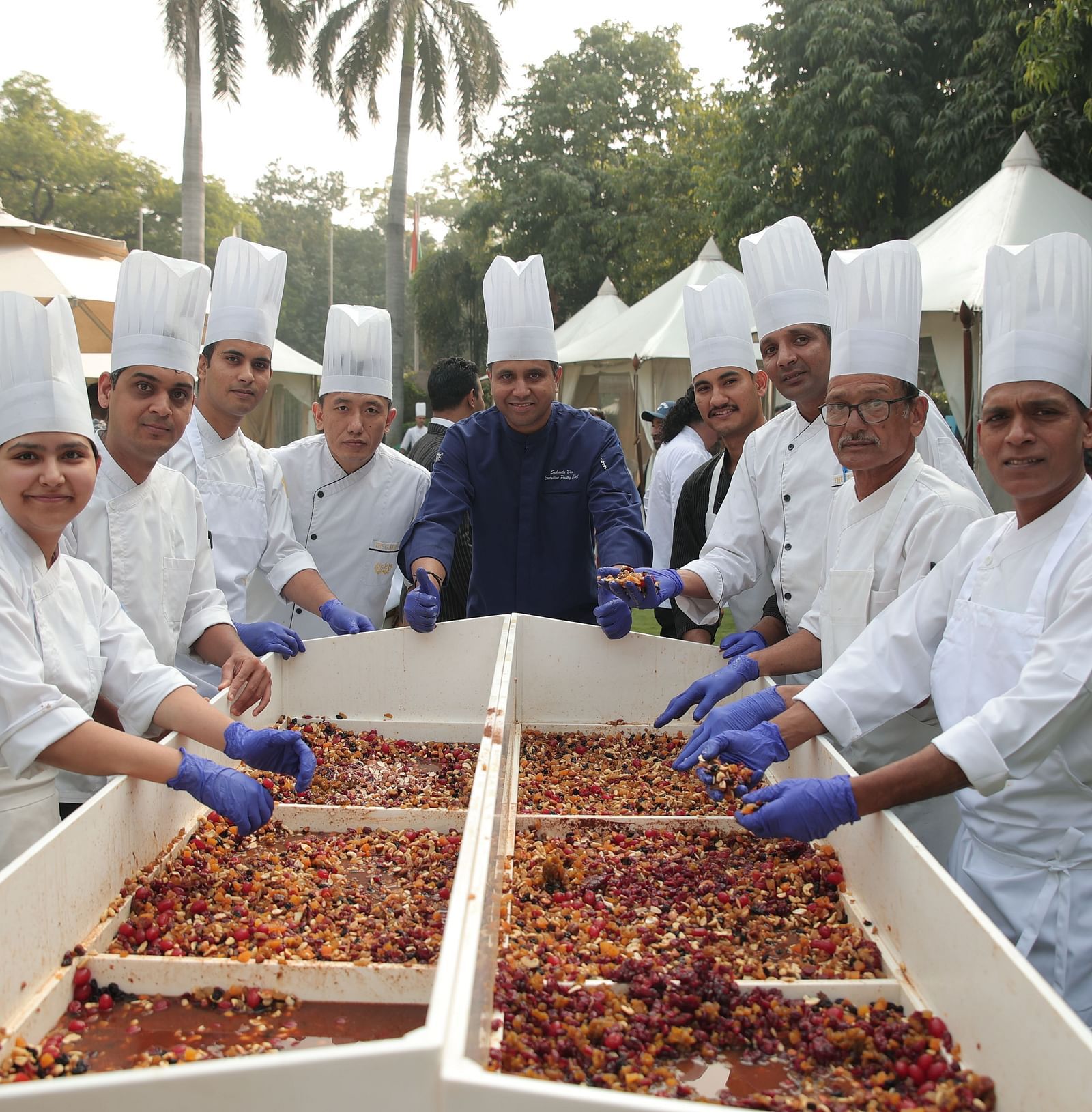 Image of people posing for a photo while preparing a cake in the open, spacious garden at The Claridges New Delhi