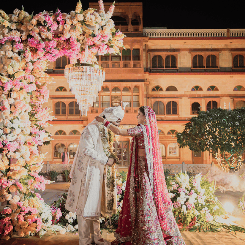A couple in their wedding attire standing at the wedding alter with Umaid Palace, a royal wedding palace venue as their background.