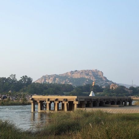 Hampi stone pavilion by river with rocky hills.