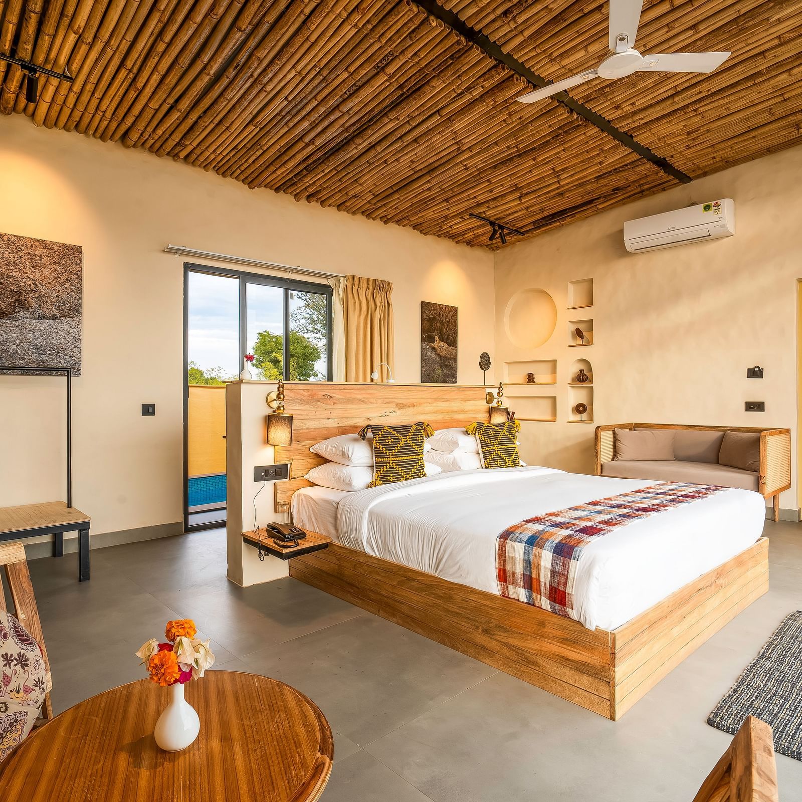 An image of a wooden furnished bedroom  featuring a double size bed, a  chair and centre table, a sofa, AC, fan,  and some decorative items - Kurja Jawai