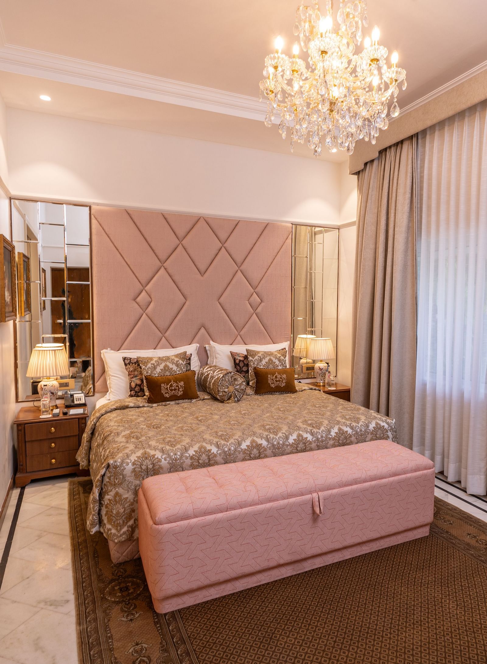 Luxury Suite at The Claridges New Delhi, featuring a cosy king sized bed with pillows and an elegant chandelier hanging overhead