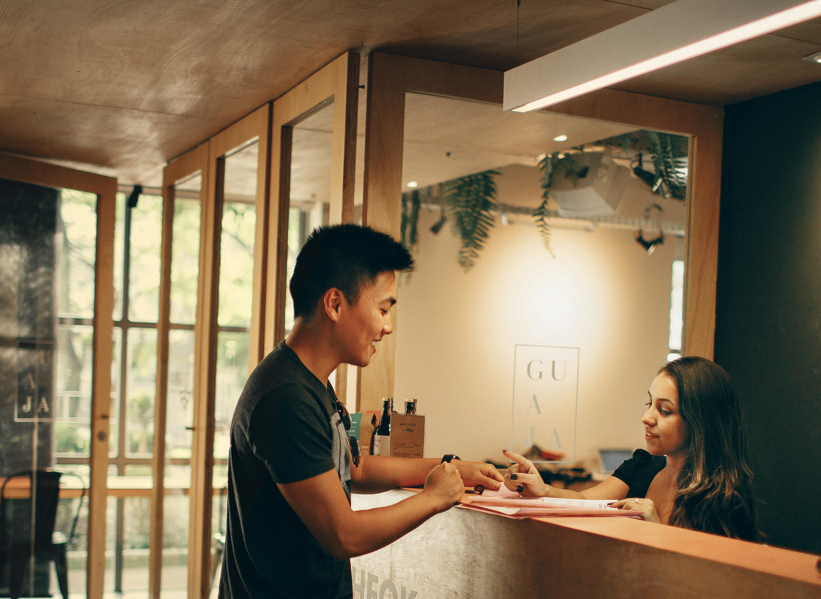 A person standing in front of a reception desk in conversation with a woman attending to his queries.