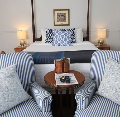 Seating area with striped chairs, tray table and showcasing a king size bed in the background at Hartstone Inn