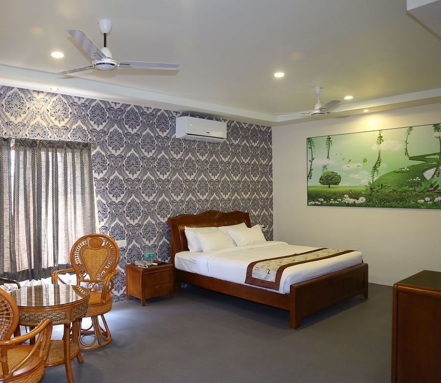Bedroom of the Themed Villa furnished with a wall-mounted AC, king size bed, sitting bench, wall-mounted AC and curtained windows at GK Hill View Resort.