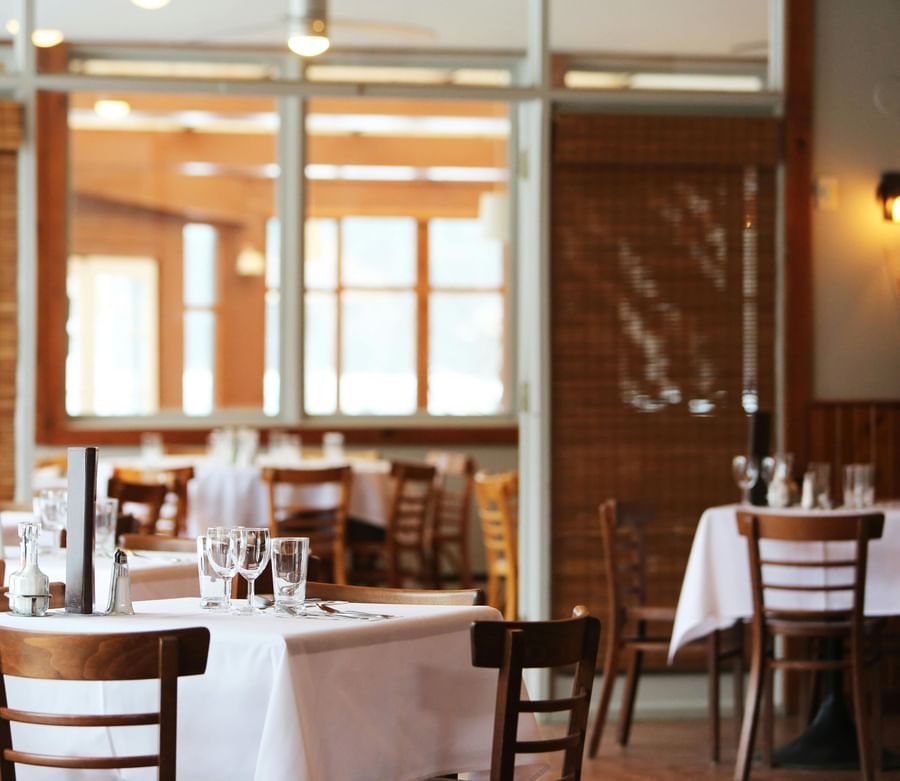 A bright restaurant interior with wooden chairs and windows.