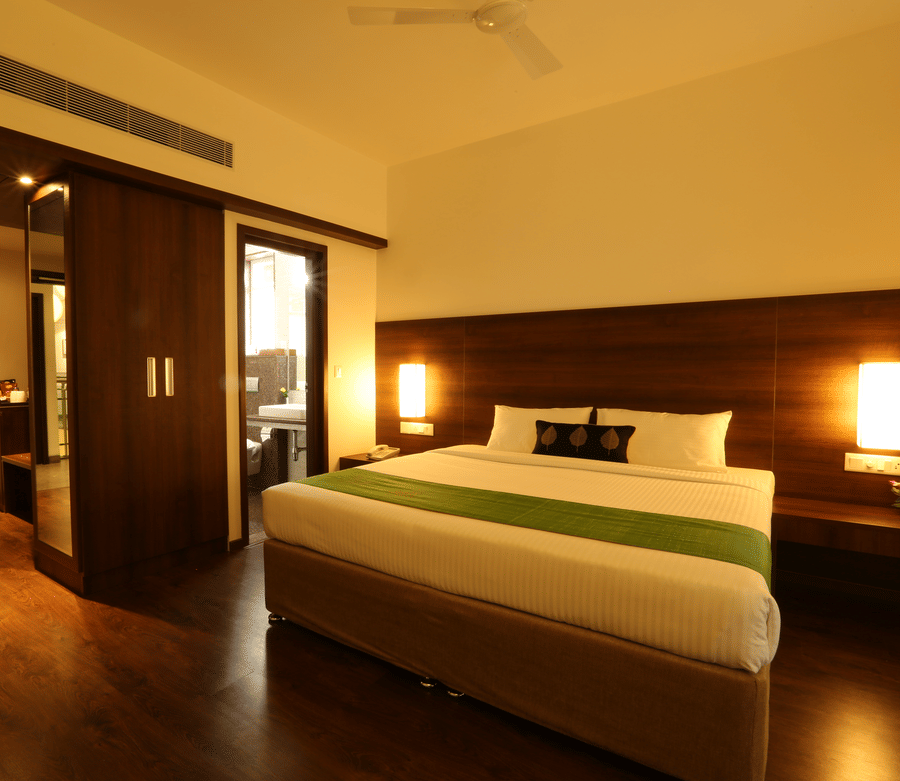 A spacious Executive Room featuring a bed with green runner, dark wood panelling, warm bedside lights, and wooden flooring at Temple Tree Hotel, Bangalore.