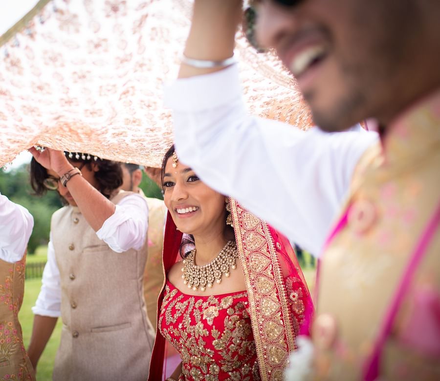 a woman dressed in a red attire walking along with people holding her veil