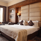 Premium Rooms at The Bristol Hotel Gurgaon, with a large bed, spreads, pillows, lamps, a window, a table and a cushion.