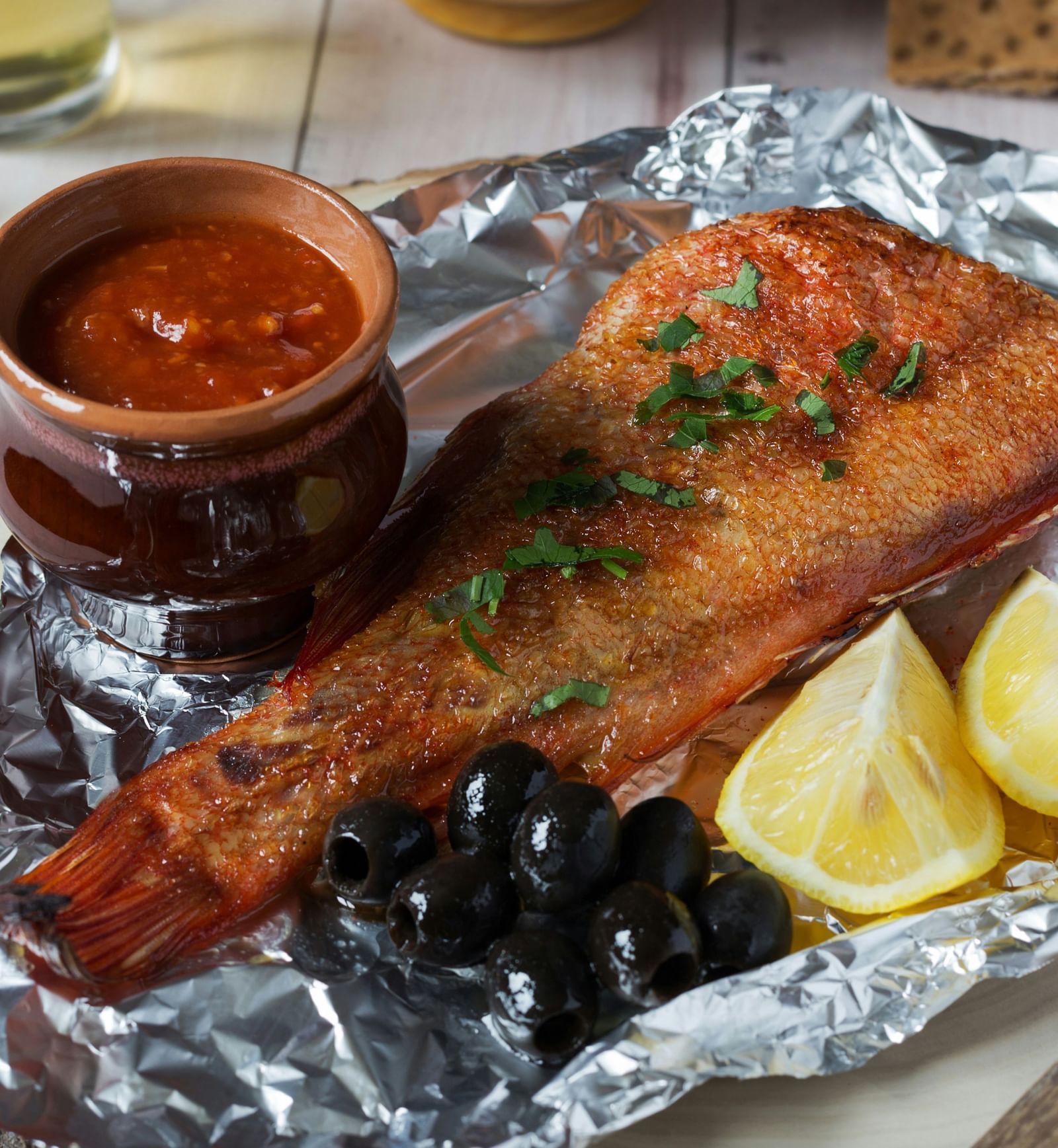 A fish's bottom half in an aluminium foil with a dip next to it kept on a plate| Mango Hill, Pondicherry