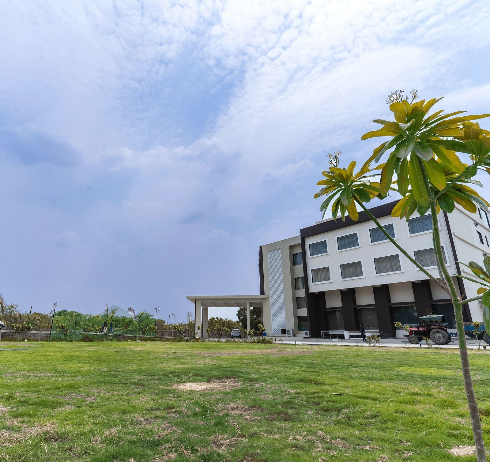 A wide-angle shot of a Bamboo Saa Mulberry Resort, Pushkar with palm trees and a lawn in front of it.