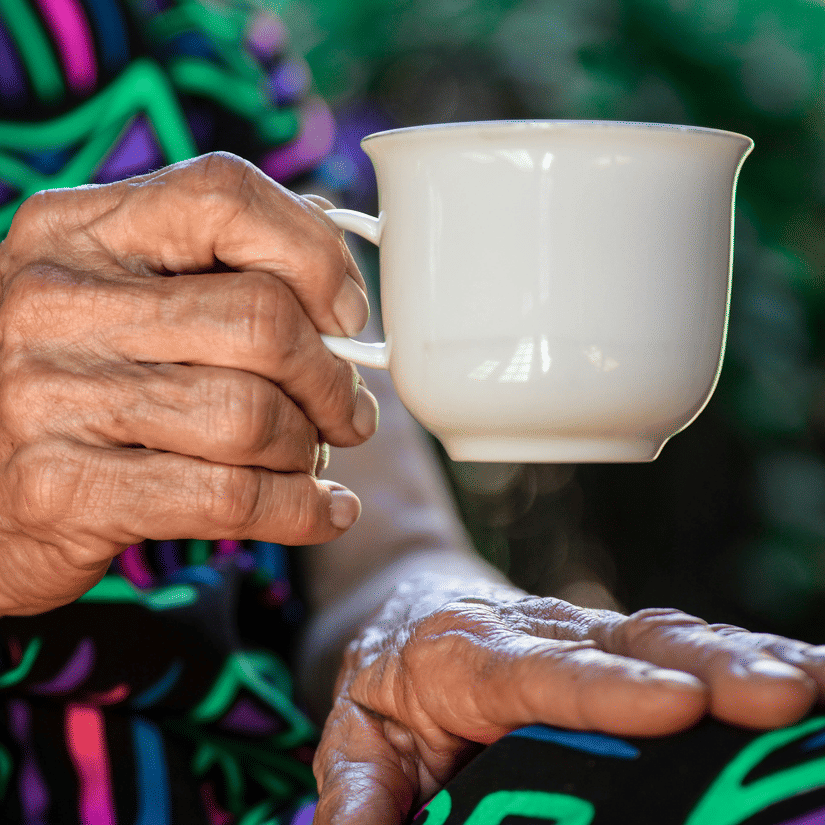 An elderly woman drinking a cup of coffee.