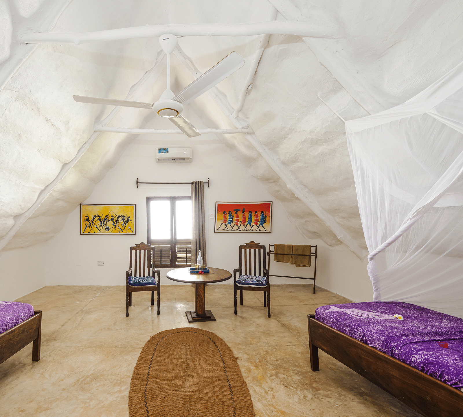 A cosy room with a wooden bed and a table with chairs with windows in the background offering natural light in Sea View Family Cottages - Shooting Star Boutique Hotel.