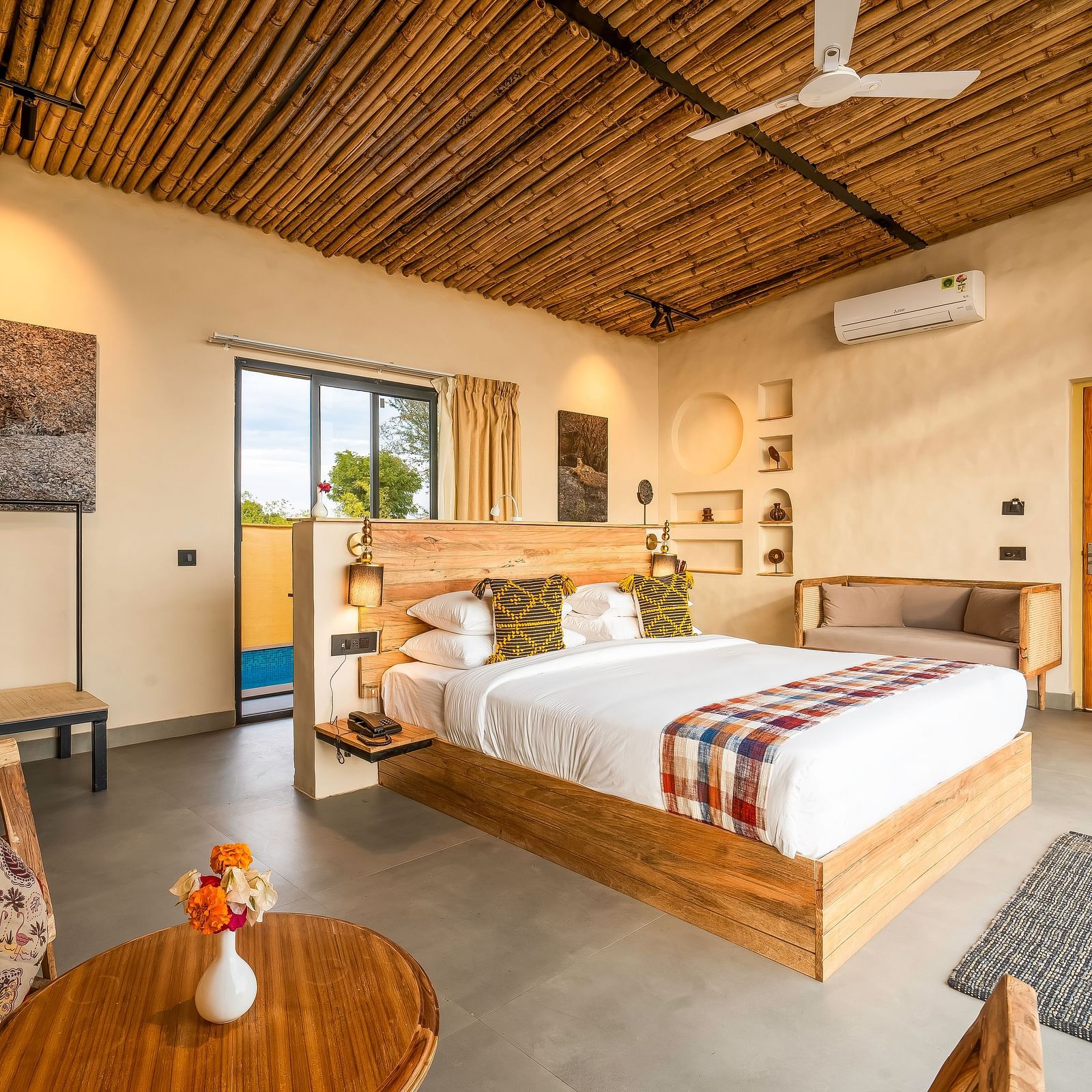 An image of a wooden furnished bedroom  featuring a double size bed, a  chair and centre table, a sofa, AC, fan,  and some decorative items - Kurja Jawai