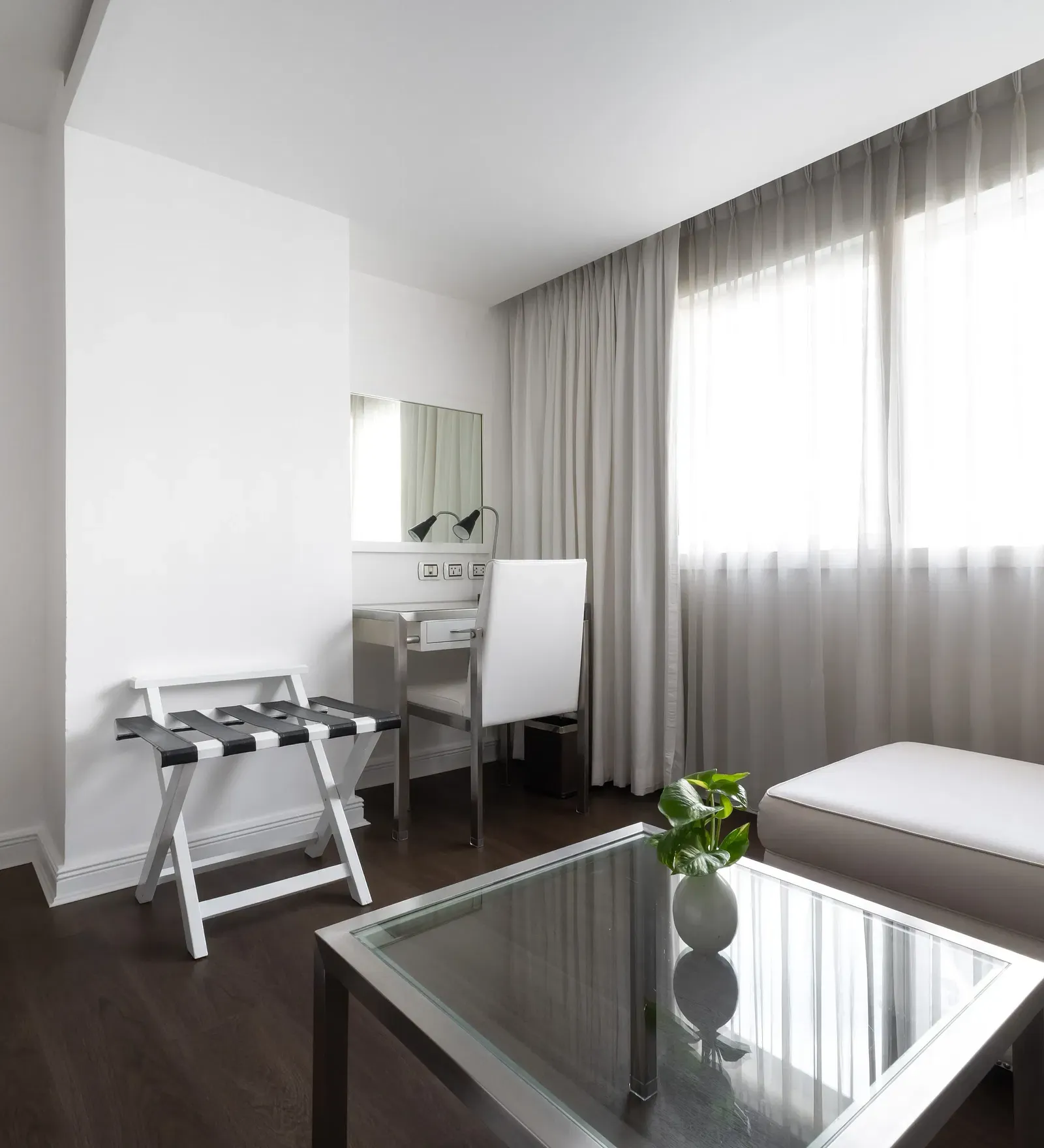 Minimalist hotel workspace with white desk, black checkered chair, cream sofa, glass table, and neutral decor creating a sophisticated ambience at Night Hotel Bangkok.
