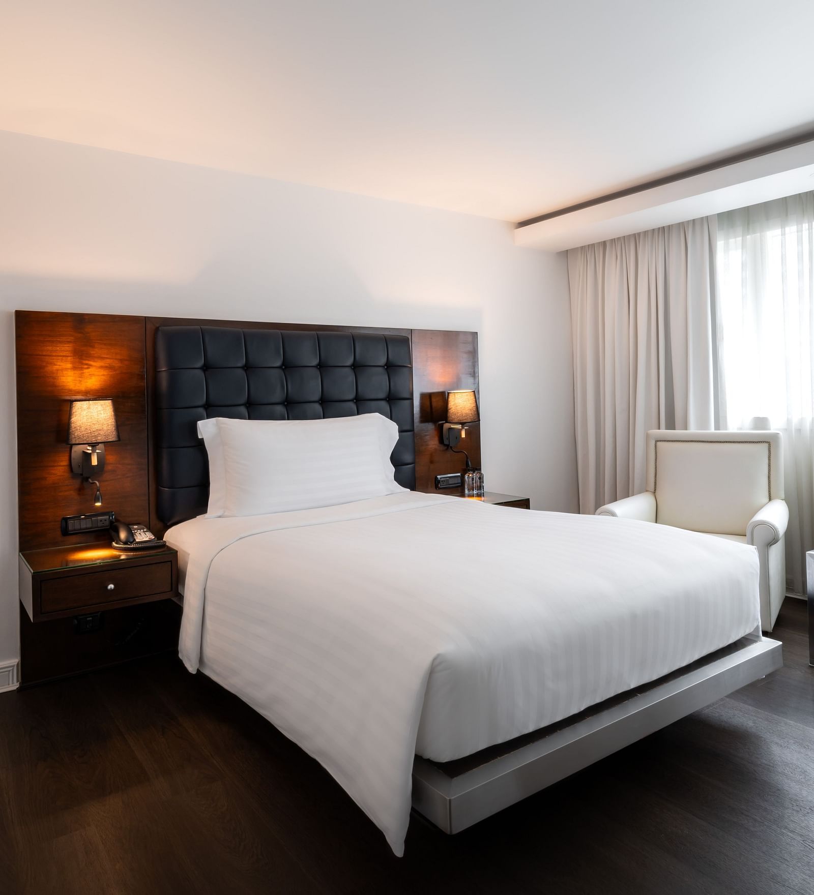 Minimalist bedroom with dark headboard, white linens, and window seating at Night Hotel Bangkok.