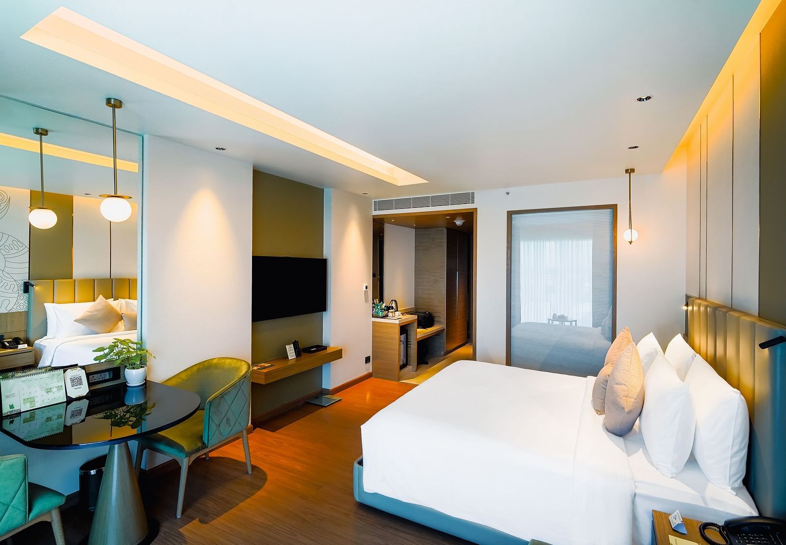 An image of a room with a large bed, work desk, and a wall-mounted television