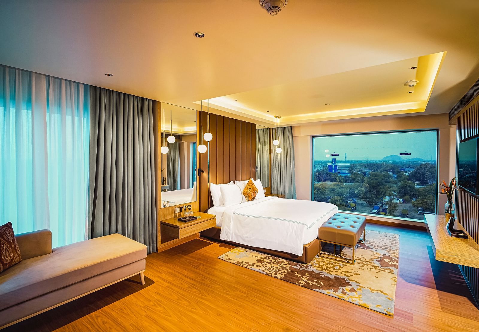A beautiful image of a hotel room in Madurai with a large bed, a couch, and a wall-mounted television