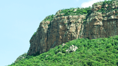 an open mountain with greenery below and above it and blue sky in the background