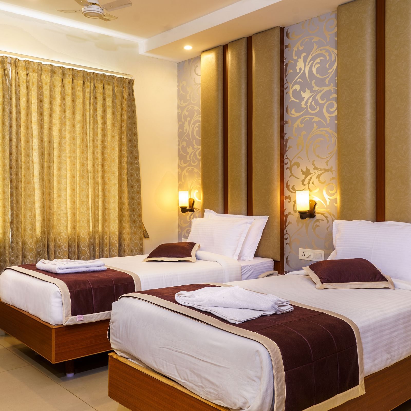 A bedroom at Wyt Hotels, Rameswaram featuring twin beds, a chair, and bedside tables with lamps for both beds.