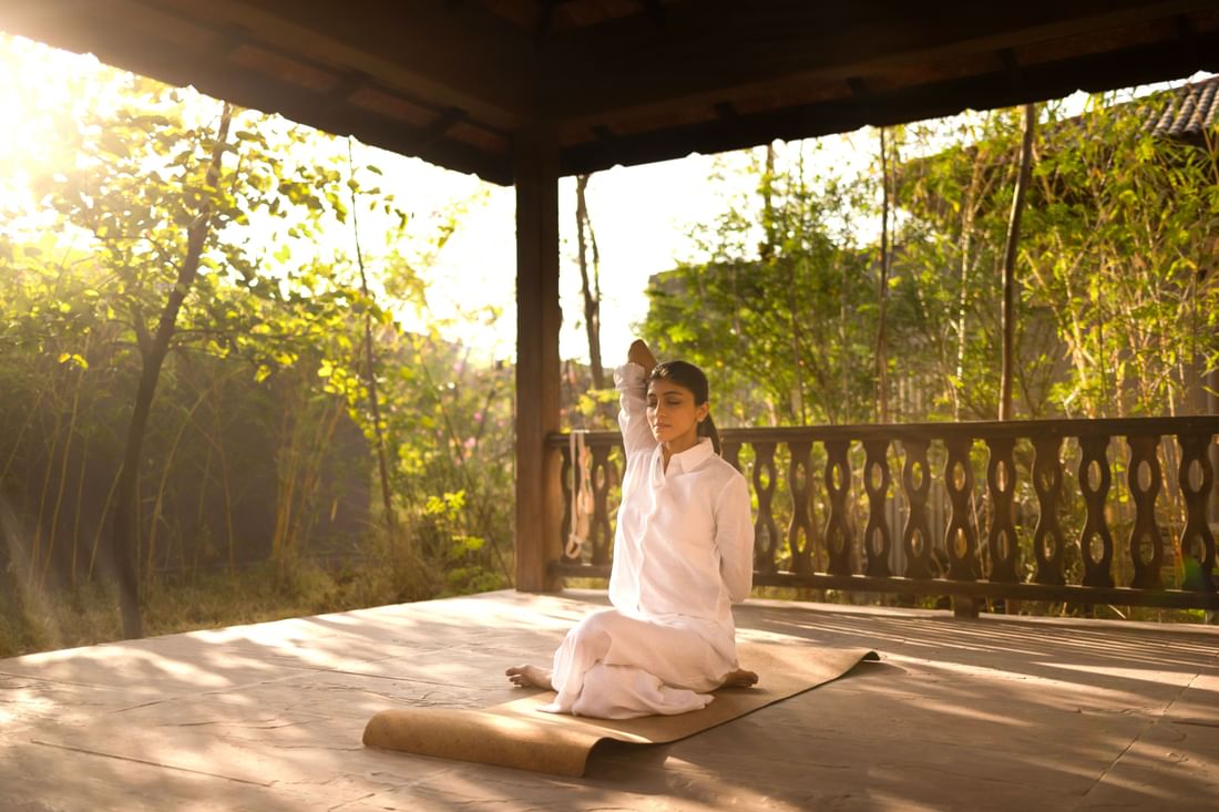 A guest meditates peacefully in an open-air pavilion at Aramness, surrounded by tranquil forest greenery.