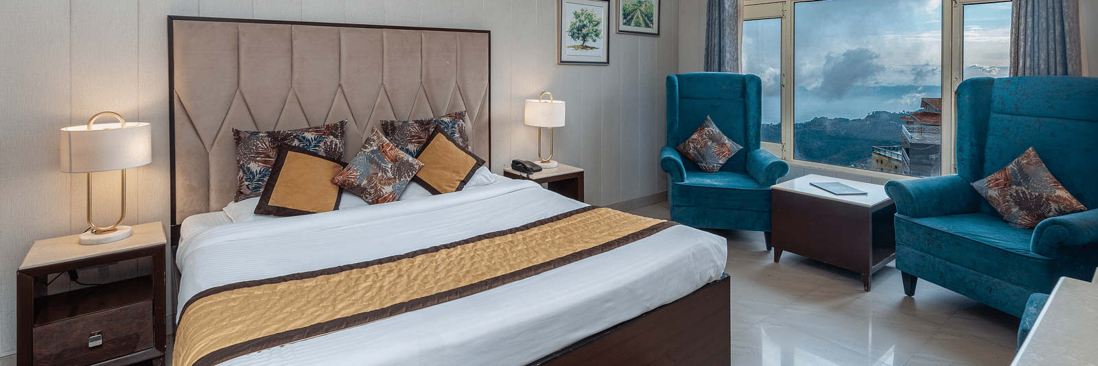 The image shows a hotel room with a large bed, two blue armchairs, a coffee table, and a window with a view | DLS The Pearl