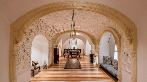 A hallway with arched doorways, a wooden floor, and a hanging structure in Tijara Fort-Palace - 19th Century, Alwar.