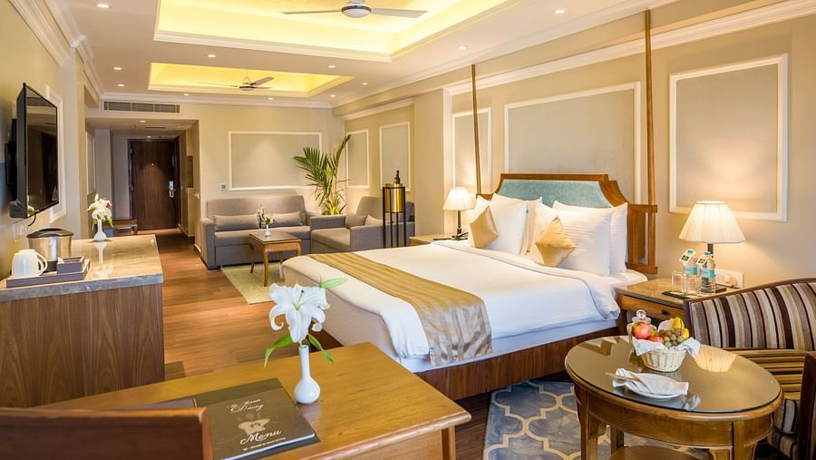 Spacious bed with a wall-mounted TV opposite it and a large window covered by curtains.