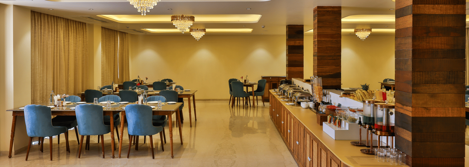 A wide interior shot of the dining area showing the long wooden buffet counter and elegant chandeliers - Tathastu Chavri Resort, Jawai