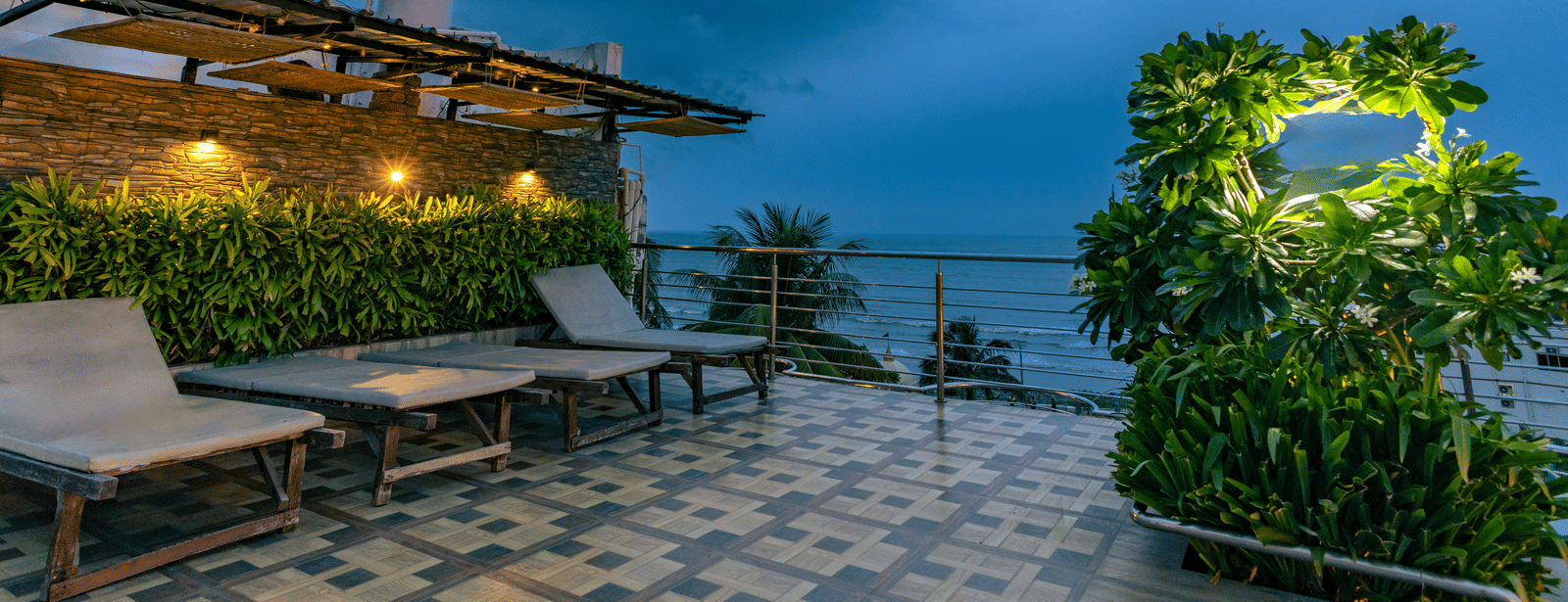 An outdoor seating area with tables, sun loungers, plants and a cloudy sky at Hotel Seagull Digha.