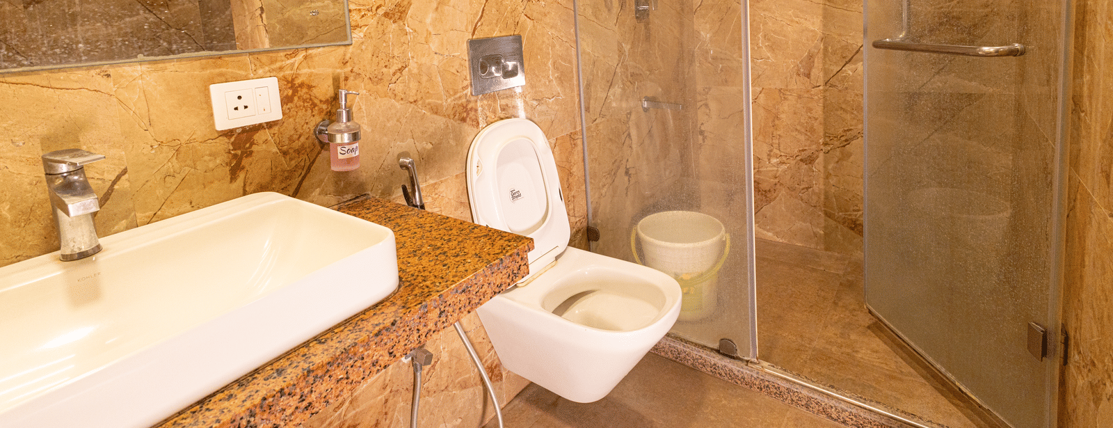 A bathroom with a sink, mirror, toilet, and glass-enclosed shower area at Hotel Seagull Digha.