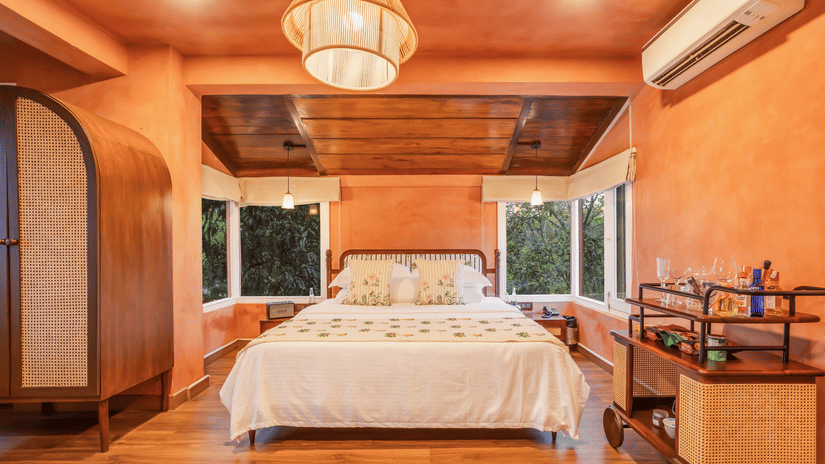 View of the Penthouse at Unseen Boutique Hotel Assagao Goa with a king bed, rattan pendant light, wooden ceiling, and warm natural light.