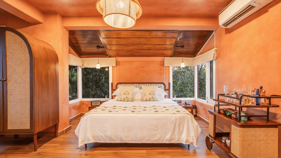 View of the Penthouse at Unseen Boutique Hotel Assagao Goa with a king bed, rattan pendant light, wooden ceiling, and warm natural light.