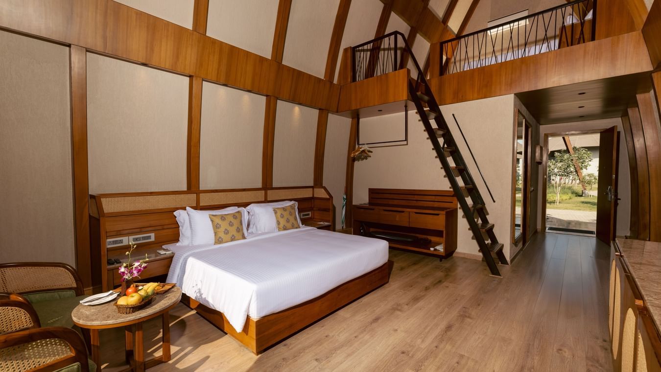 an interior of a bamboo villa with a king size bed and a stairs to the second deck at Ananta Spa and Resort, Ajabgarh