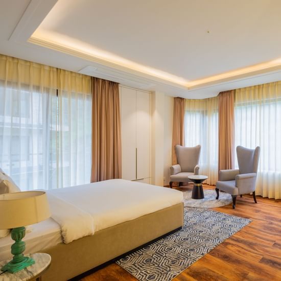 Spacious guest suite with large windows, warm wooden flooring, and a clean, modern design, displaying the elegant accommodation options at The Manor Sports & Wellness Hotel in Shimla.