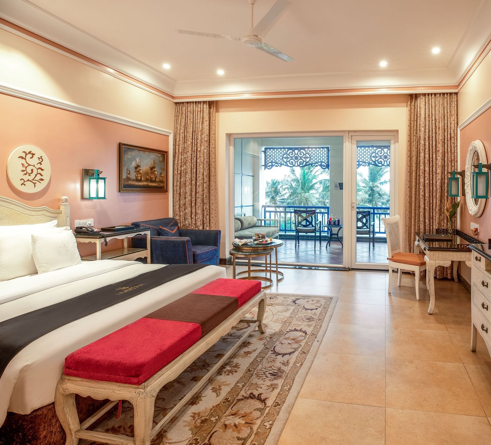 Spacious bedroom with seating area, a workstation, a ceiling fan, a wall-mounted TV, and large glass windows at MAYFAIR Palm Beach Resort, Gopalpur-On-Sea