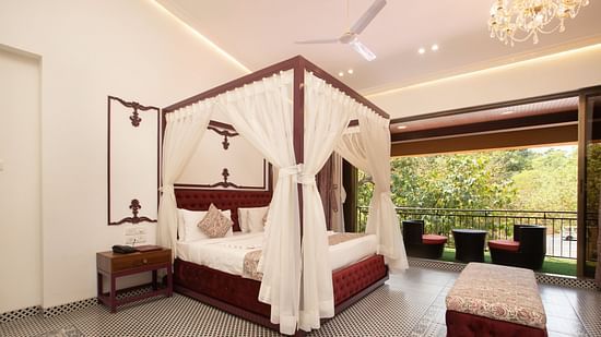 Royal Suite at Zara's Resort with a four-poster bed, white drapes, patterned flooring, and balcony seating overlooking lush green trees outside.