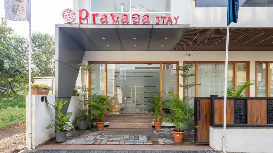 Facade and entry to Pravasa Stay Vijay Nagar, Indore, lined by potted plants on both sides, and an illuminated logo placed on the elevated ceiling.