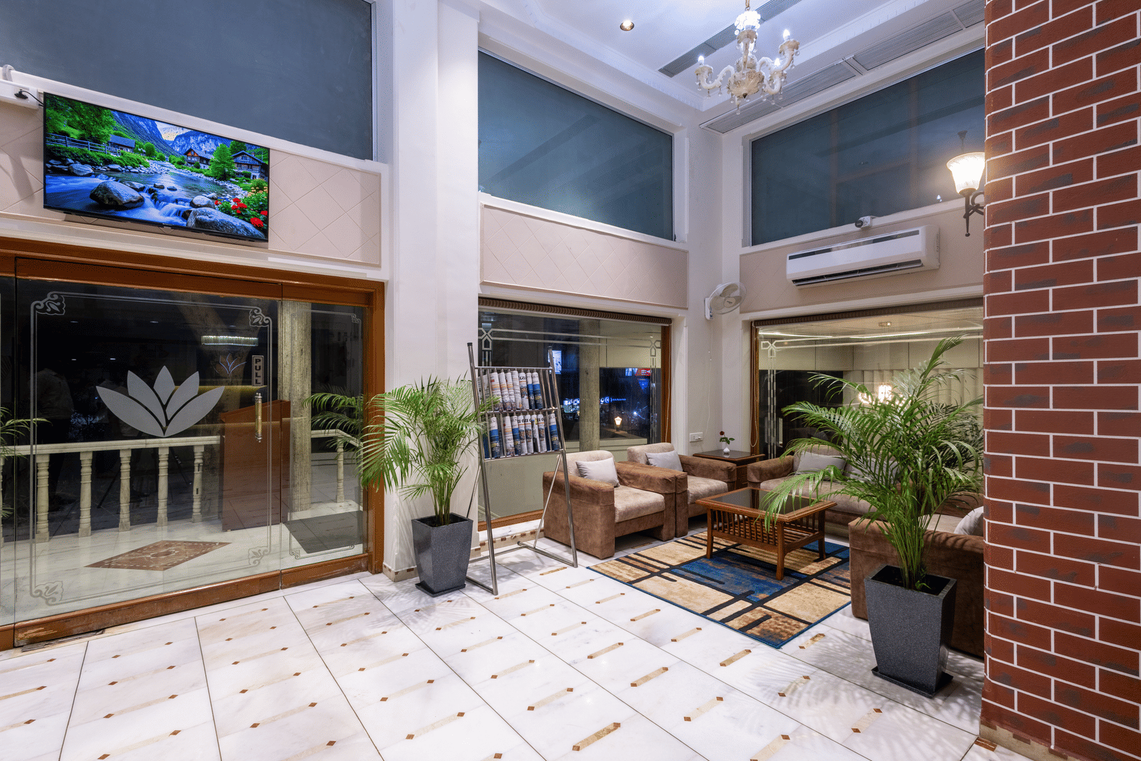 View of a patio/courtyard area with seating and plants, looking towards the hotel interior through glass doors at Pravasa Stay, Vadodara.