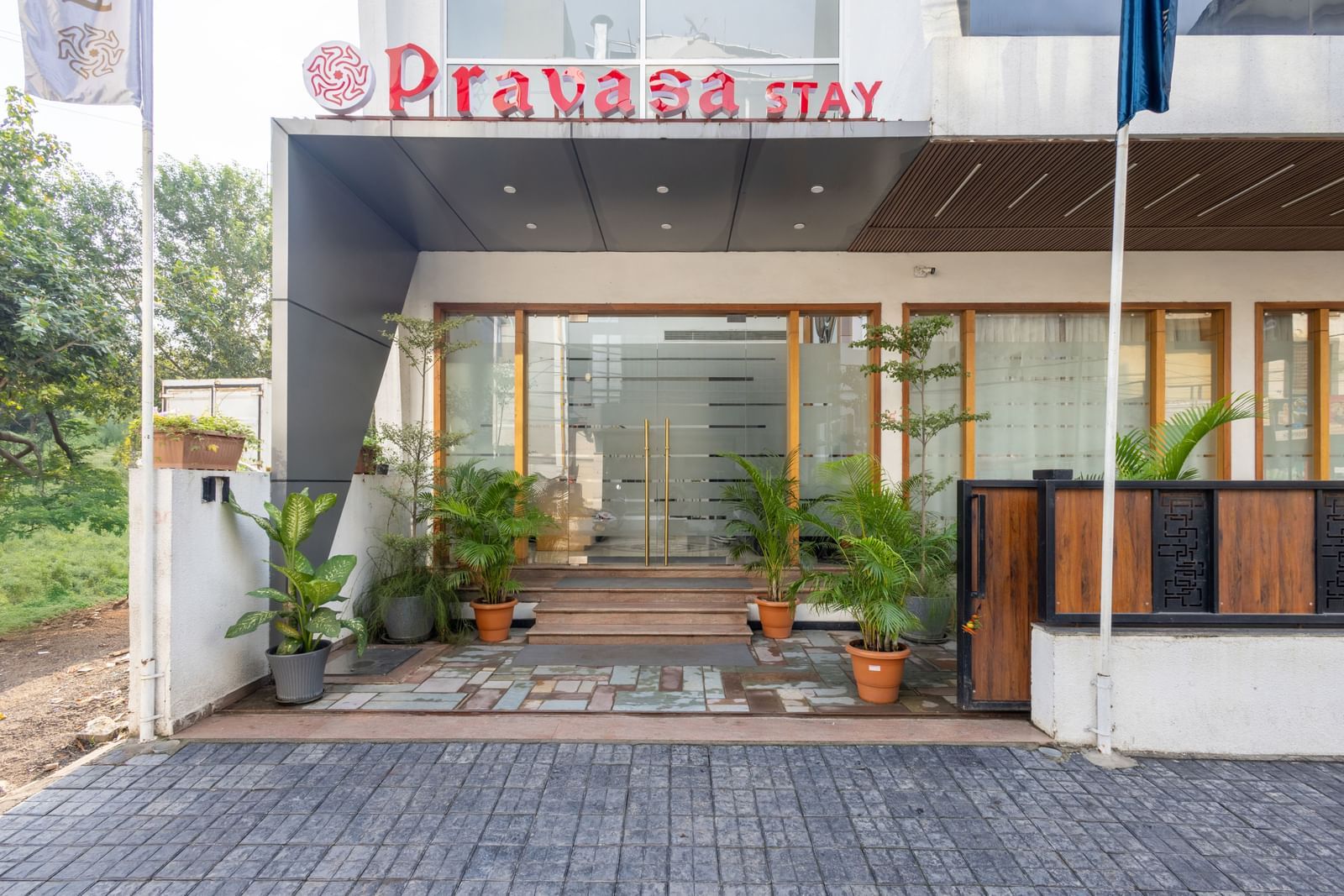 Facade and entry to Pravasa Stay Vijay Nagar, Indore, lined by potted plants on both sides, and an illuminated logo placed on the elevated ceiling.