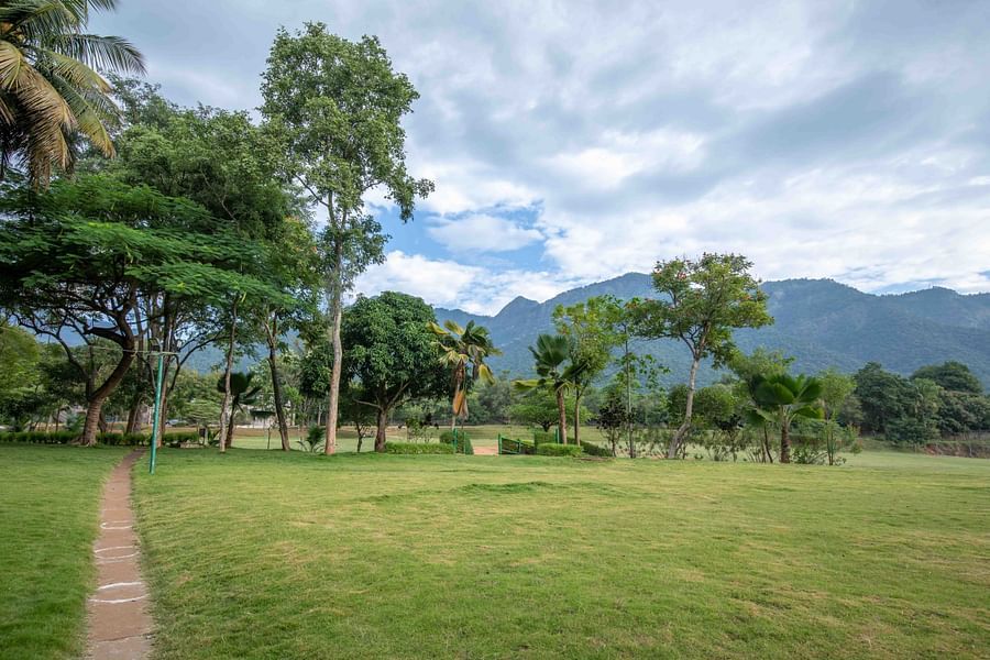 Large open lawn with a pathway leading into the distance, surrounded by trees and mountains in the background - Black Thunder, Coimbatore
