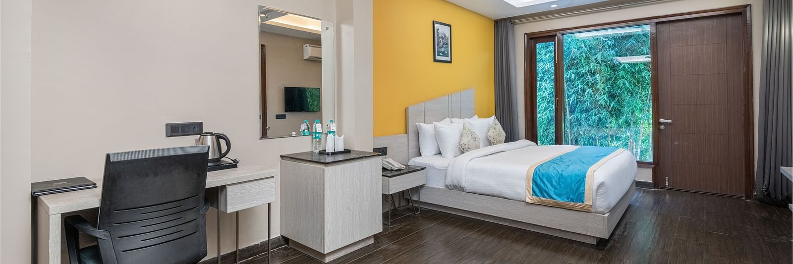A spacious room at DLS Forest Vines Resort featuring a large bed, glass windows, a desk, and a chair.