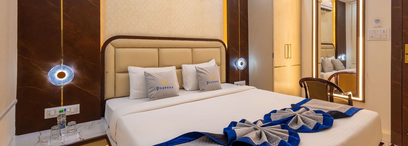 A well lit room with a double bed, side tables, mirror with a chair, and air conditioning at Pravasa Stay Dewas Naka, Indore.