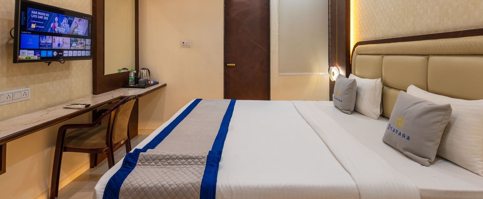 Room with a double bed, wall-mounted TV & a chair, and ceiling fan at Pravasa Stay Dewas Naka, Indore.