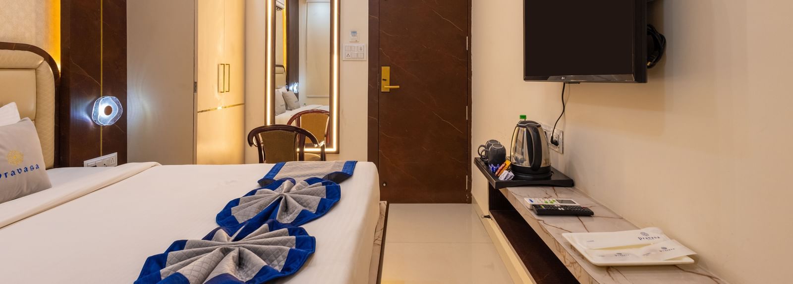 Room featuring a double bed, wall-mounted TV, a mirror with a chair, and wardrobe at Pravasa Stay Dewas Naka, Indore.